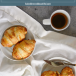 2 croissants on a white table runner with a small coffee mug filled with black coffee on a blue background