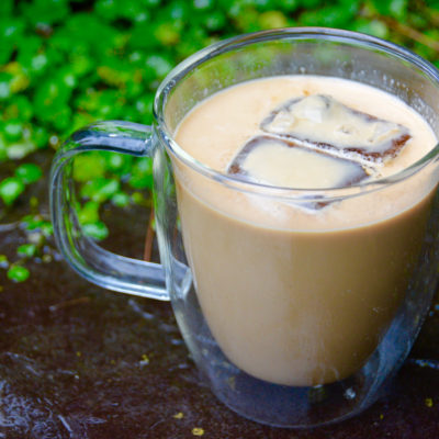 clear mug of iced coffee on pavement with greenery