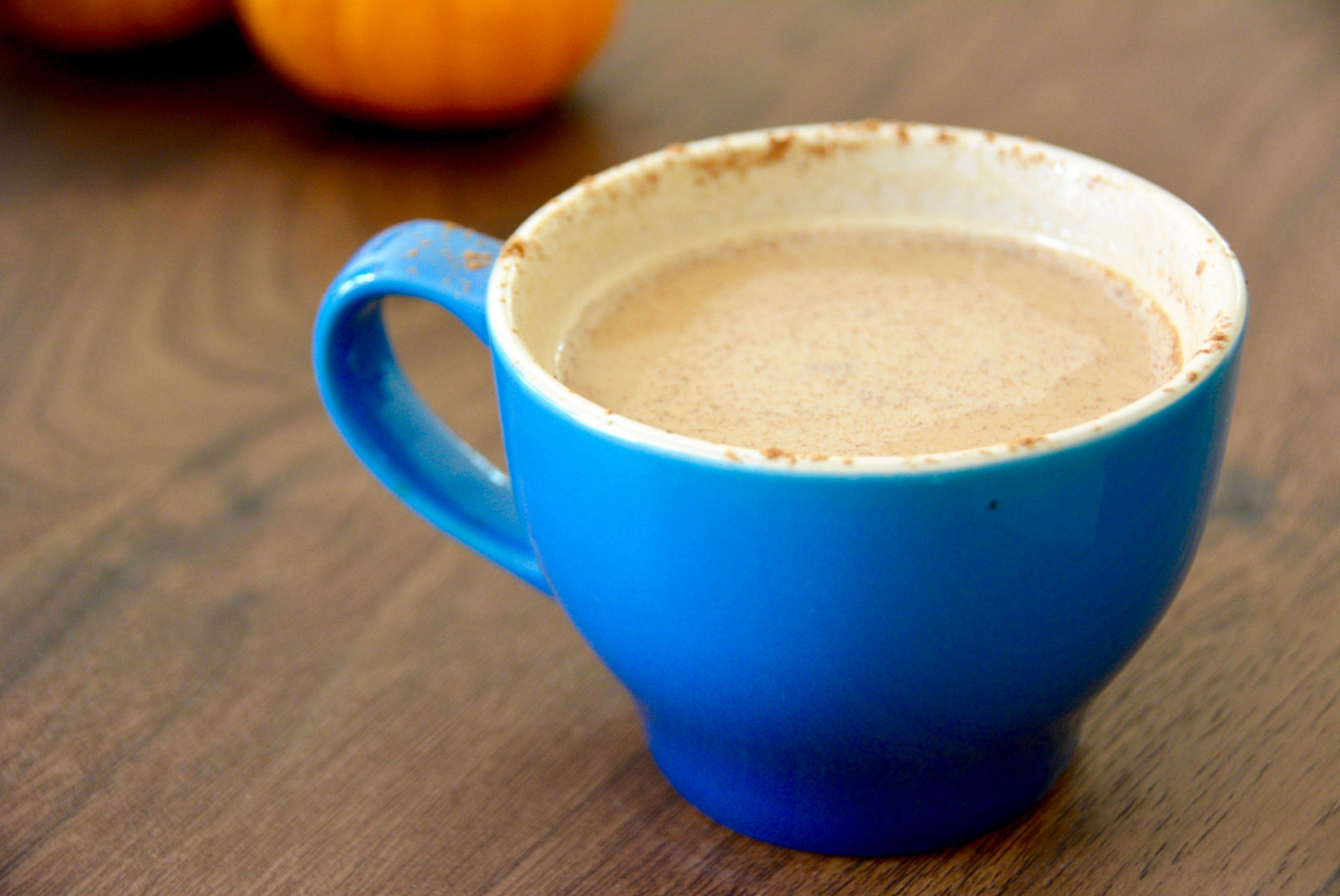 pumpkin spice latte in a blue coffee mug on a wooden table with pumpkins in background