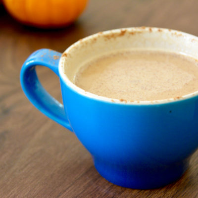 pumpkin spice latte in a blue coffee mug on a wooden table with pumpkins in background