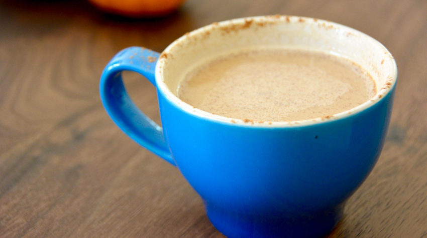 pumpkin spice latte in a blue coffee mug on a wooden table with pumpkins in background