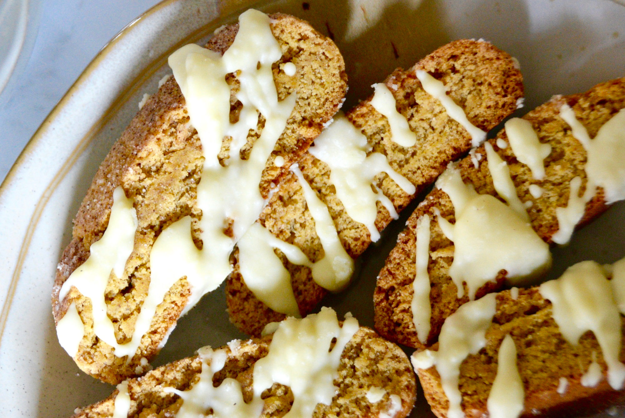 pumpkin biscotti drizzled with white chocolate on a light pink speckled plate