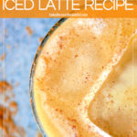 from top - view of pumpkin spice latte in a high ball glass with a blue background a small pumpkin and two ice cubes in the latte