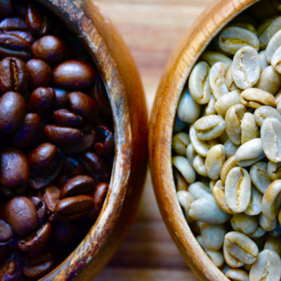 two wooden bowls filled with green beans and roasted coffee beans