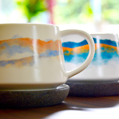 his and hers ceramic coffee mugs on a wood table with a floral background