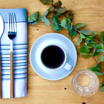 coffee mug on a white saucer on a wood background with eucalyptus