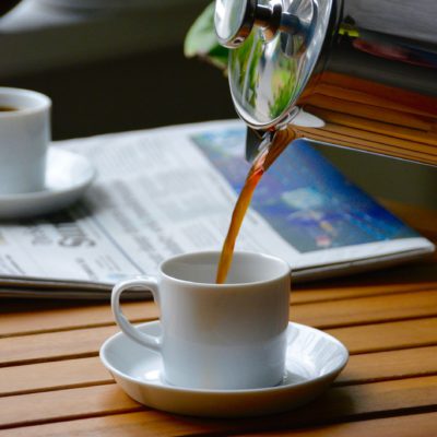 french press coffee being poured into a mini mug next to a newspaper