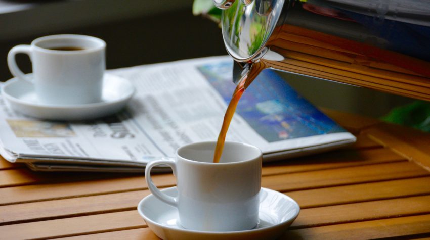 french press coffee being poured into a mini mug next to a newspaper